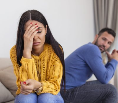 Sad pensive young girl thinking of relationships problems sitting on sofa with offended boyfriend, conflicts in marriage